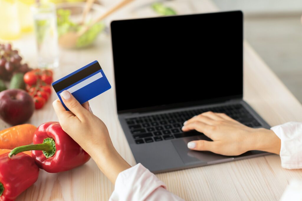 Woman using laptop with in kitchen, holding credit card